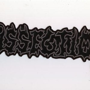 Op de afbeelding: Een zwart geborduurd embleem met het woord "DISSECTION" in een gestileerd, gotisch lettertype. De tekst is grijs omlijnd, met een zwarte vulling. Het embleem heeft een decoratieve, gekartelde rand.
