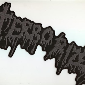 May include: A black and gray patch with the word "TERRORIZED" in a dripping, stylized font. The patch has a jagged edge and is likely for clothing or accessories.