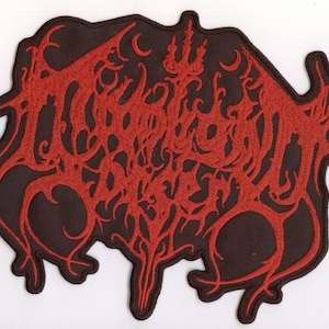 Op de afbeelding: Een rood geborduurde patch met een ingewikkeld, gestileerd ontwerp op een donkerbruine achtergrond. De patch heeft een unieke, onregelmatige vorm en heeft een complex, wervelend patroon. Het ontwerp is gedetailleerd en opvallend.