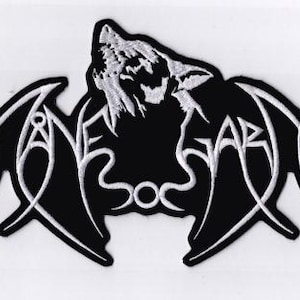 May include: Black and white embroidered patch featuring a howling wolf and the word "ANEBAR" in stylized lettering. The patch has a unique, symmetrical design with curved lines and a wavy border, suitable for jackets or bags.
