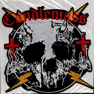 Può includere: Toppa ricamata con il nome della band "Candlemass" in lettere gotiche rosse. Il design include un teschio, croci rosse e fulmini gialli su sfondo nero.