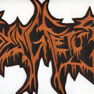 May include: A black and orange embroidered patch featuring stylized, jagged lettering that resembles a death metal band logo. The design has sharp, pointed edges and a dripping, textured appearance with a dark background and vibrant orange thread.