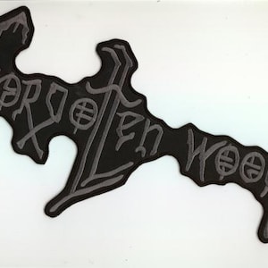 Op de afbeelding: Een zwarte patch met de woorden "Forgotten Woods" in grijze, gestileerde letters. De patch heeft een unieke, onregelmatige vorm met afgeronde randen. De tekst bevat decoratieve symbolen in de letters.