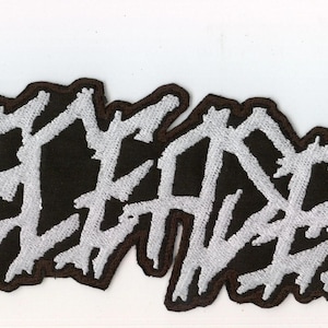 Könnte beinhalten: Ein schwarz-weiß bestickter Aufnäher mit dem Wort DECEASED in einer gezackten, stilisierten Schriftart. Die Buchstaben sind mit weißem Garn auf einem dicken schwarzen Rand gestickt, was ein kontrastreiches Design für Textilien ergibt.