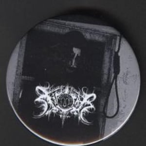 May include: A circular button in monochrome tones, featuring a gothic design. The button displays a dark image of a person and a noose, with a white, ornate logo at the bottom. The button has a dark, moody aesthetic.