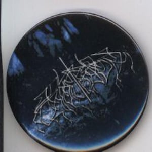 May include: A dark blue ceramic plate with a white, abstract design. The plate has a glossy finish and a slightly raised edge. The design appears to be hand-painted or etched onto the surface.