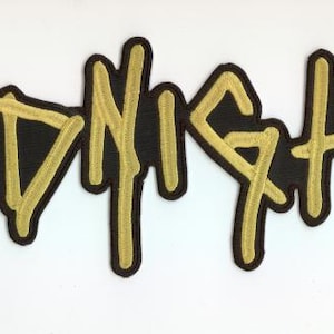 Peut inclure: Écusson brodé avec le mot "MIDNIGHT" en lettres dorées sur fond noir. Le patch a une bordure noire et est probablement conçu pour être cousu ou repassé sur des vêtements ou accessoires.