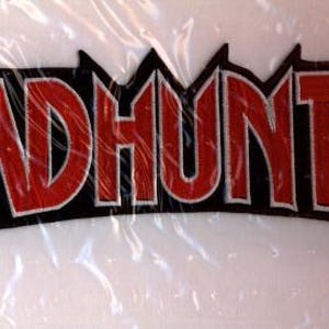 Könnte beinhalten: Ein rot-schwarzer Aufnäher mit dem Wort "HEADHUNTER" in fetter, stilisierter Schrift. Die Buchstaben sind rot mit weißer Umrandung, vor schwarzem Hintergrund. Der Aufnäher hat einen gezackten, dekorativen Rand.