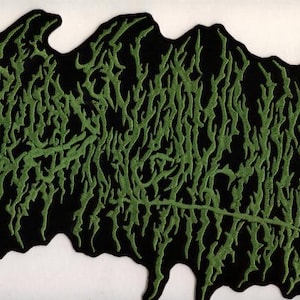 May include: A black patch with a green, stylized, organic design. The green design appears to be an abstract representation of a plant or a root system. The patch is likely for clothing or accessories.