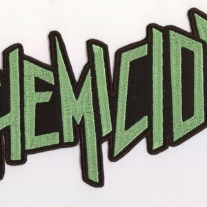 May include: Embroidered patch with the word "CHEMICIDE" in stylized, blocky, green letters. The letters are outlined in black and set against a black background. The patch is likely for clothing or accessories.