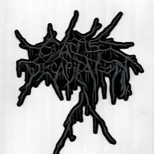 May include: A black and gray embroidered patch with the word "DECAPITATED" in a stylized font. The patch features a dark, organic design resembling roots or branches, with a dripping effect. The patch is likely for clothing or accessories.