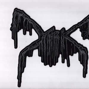 Könnte beinhalten: Ein schwarzer Aufnäher mit einem symmetrischen Design, möglicherweise eine Fledermaus oder ein Insekt, mit tropfenden, strukturierten Details. Das Design ist vor einem weißen Hintergrund platziert und erzeugt einen hohen Kontrast.