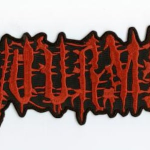 May include: A rectangular patch with the word "DEVOLVEMENT" embroidered in red thread on a black background. The letters have a dripping, jagged style, and the patch has a black border.