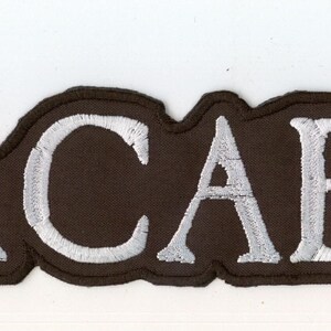 Op de afbeelding: Een rechthoekige geborduurde patch met het woord MACABRE in witte hoofdletters met een donkerbruine rand. De letters zijn gestikt in een schreeflettertype en de hele patch heeft een donkerbruine achtergrond met een bijpassende gestikte rand.