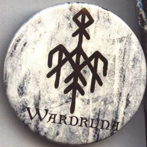 May include: A round, white button with a textured, marbled appearance. A dark brown, stylized symbol is centered on the button, with the word "WARDRUDA" printed in a serif font below the symbol.