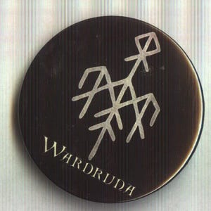 Puede incluir: Un objeto circular marrón oscuro con un símbolo estilizado plateado y la palabra "WARDRUDA" en una fuente plateada a juego. El símbolo es una representación geométrica.