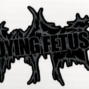 Può includere: Toppa nera con la scritta "DYING FETUS" in grassetto. La toppa ha una forma irregolare unica con un design testurizzato e gocciolante attorno al testo, creando un effetto visivo sorprendente. Ideale per abbigliamento o accessori.