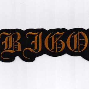 Puede incluir: Un parche negro bordado con la palabra "ARBOR" en letras góticas doradas. El parche tiene un borde ondulado e irregular. Está diseñado para ser cosido en ropa o accesorios.