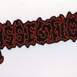 Op de afbeelding: Zwart geborduurd embleem met het woord "DESECRATED" in rode, vlamachtige letters. De letters zijn rood met een zwarte achtergrond, wat een gedurfd contrast creëert. De patch heeft een unieke, gekartelde rand.