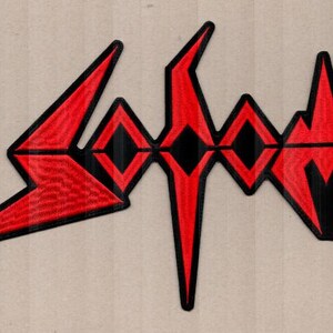 Può includere: Toppa ricamata rossa e nera con un logo stilizzato. Il design presenta angoli acuti e forme geometriche, creando un forte impatto visivo. Adatta per abbigliamento o accessori.