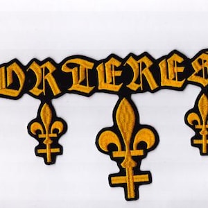 May include: Embroidered patch featuring the word "FORTRESSE" in yellow gothic lettering on a black background. Three yellow fleur-de-lis symbols are suspended beneath the text, forming a decorative design.