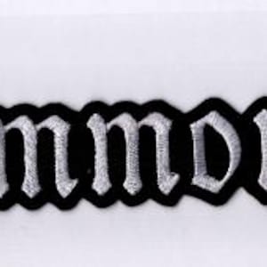 Puede incluir: Un parche bordado rectangular que presenta la palabra Summoning en una fuente de estilo gótico blanca con un borde negro grueso. Las letras están cosidas con hilo texturizado, creando una apariencia en relieve sobre el fondo de tela negra.