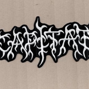 Puede incluir: Parche bordado en blanco y negro con la palabra "DECAPITATED" en una fuente gótica estilizada. El parche tiene un fondo negro con letras blancas intrincadas y elementos decorativos.