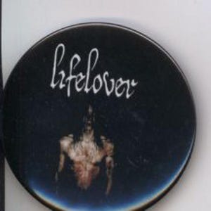May include: A circular black badge featuring the word "lifelover" in white cursive script. Beneath the text is a blurred image of a person. The badge has a dark, atmospheric design.