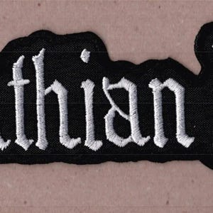 May include: A black embroidered patch featuring the text Carpathian Forest in a white gothic-style font. The patch has a die-cut border that follows the shape of the lettering, creating a distinct contrast between the white thread and black fabric.