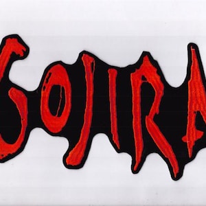 May include: A black patch featuring the word "GOJIRA" in red, with a dripping font style. The embroidered letters stand out against the black base. This patch is designed for application on clothing or accessories.