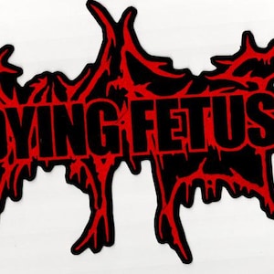 Op de afbeelding: Zwarte patch met de tekst "DYING FETUS" in vette, zwarte letters. De tekst is omlijnd met een grillig, rood ontwerp dat doet denken aan druipend bloed. De patch heeft een ongewone, onregelmatige vorm.