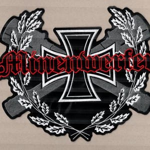 Könnte beinhalten: Gestickter Aufnäher mit einem schwarz-weißen Eisernen Kreuz-Design und dem Wort "Minenwerfer" in roter Schrift. Das Design wird von einem Lorbeerkranz umrahmt, was ein auffälliges Emblem ergibt.