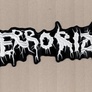 May include: Black and white embroidered patch with the word "TERRORIZE" in a stylized, gothic font. The patch has a jagged, irregular shape and a distressed aesthetic, suitable for jackets or bags.
