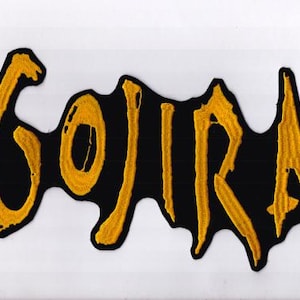 May include: Embroidered patch with the word "GOJIRA" in yellow thread on a black backing. The patch has an irregular shape, and the text is stylized. Suitable for application on clothing or accessories.