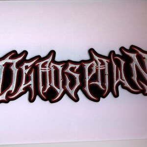 Könnte beinhalten: Gestickter Aufnäher mit dem Wort "DAWNSPAWN" in gotischer Schrift. Der Text ist weiß mit roter Umrandung und schwarzem Rand. Geeignet für Kleidung oder Accessoires.