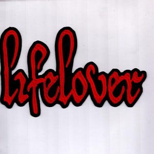 May include: A red "lifelover" patch with a black border. The word is written in a cursive style, with the letters connected. The patch is on a white background.