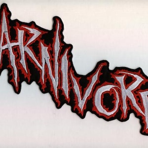May include: Embroidered patch with the word "CARNIVORE" in white, outlined in red, on a black background. The patch has a jagged, irregular shape, and the letters have a distressed, gothic style.