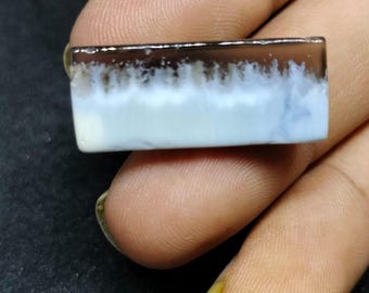May include: A rectangular, translucent, white and gray gemstone with a dark gray border. The gemstone has a cloudy, layered appearance.