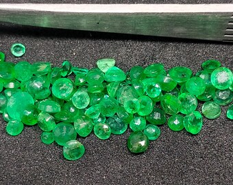 May include: A collection of green emerald gemstones, cut and polished, displayed on a dark surface.