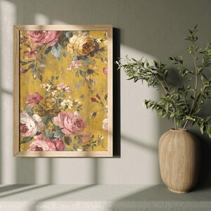 May include: A framed floral print featuring pink, yellow, and white roses on a textured yellow background. The wooden frame surrounds the artwork, which is displayed on a wall. A wooden vase with green branches is next to the framed print.