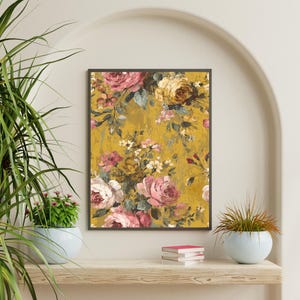 May include: A framed floral print featuring a vintage-style design. The artwork showcases a bouquet of pink, white, and yellow roses against a textured, mustard-yellow background. The print is displayed on a wooden shelf with potted plants.