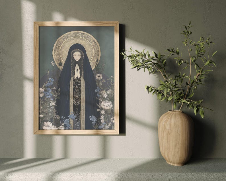 May include: A framed art print featuring a religious figure in a dark blue cloak with hands clasped in prayer. The artwork has a gold halo and is surrounded by blue and white flowers. The frame is made of light-colored wood.