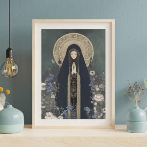 May include: Framed art print featuring a serene illustration of a figure in a dark blue veil, hands clasped in prayer. The artwork is surrounded by blue and white flowers, with a golden halo and a dark green background. The frame is light wood.