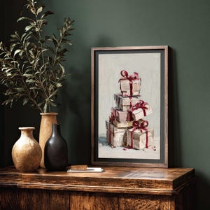May include: An oil painting depicts a stack of wrapped gifts with red ribbons. The artwork is in a dark wooden frame, resting on a wooden surface. Decorative vases and a plant are to the left of the framed art, against a dark green wall.