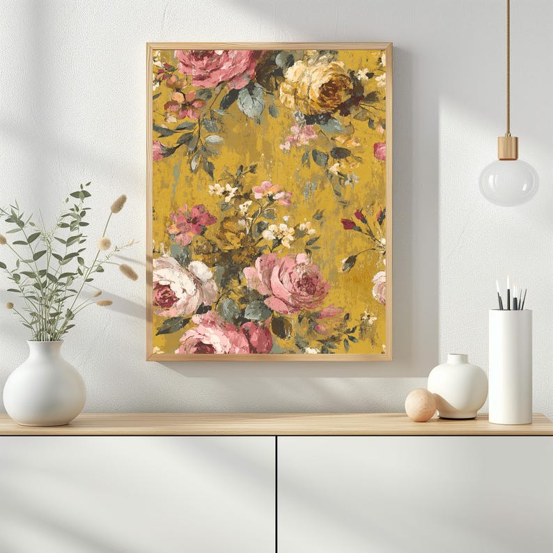 May include: A framed floral print featuring a vintage-style design. The artwork showcases a bouquet of pink and yellow roses against a textured, mustard-yellow background. The print is enclosed in a light brown wooden frame.
