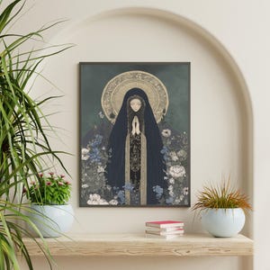 May include: A framed art print featuring a figure in a dark blue cloak with hands clasped in prayer. The artwork has a halo and is surrounded by flowers in shades of blue, white, and gray. The background is a muted teal color.