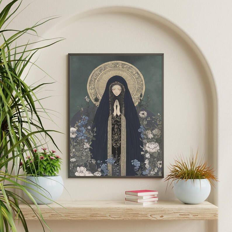 May include: A framed art print featuring a figure in a dark blue cloak with hands clasped in prayer. The artwork has a halo and is surrounded by flowers in shades of blue, white, and gray. The background is a muted teal color.