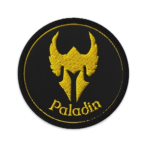 May include: Circular embroidered patch with a black base and a gold emblem. The emblem is a stylized design with an arrow shape and wing-like elements. The word "Paladin" is embroidered in gold beneath the emblem.