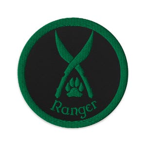 Op de afbeelding: Geborduurde patch met een groene rand. De patch heeft een zwart midden met gekruiste groene messen, een pootafdruk en het woord "Ranger" in het groen.