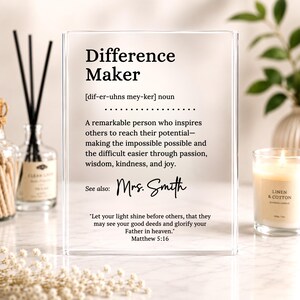May include: A clear rectangular acrylic plaque featuring black printed text that defines the term Difference Maker as a remarkable person who inspires others. It includes the name Mrs. Smith, a scripture reference to Matthew 5:16, and phonetic pronunciation.